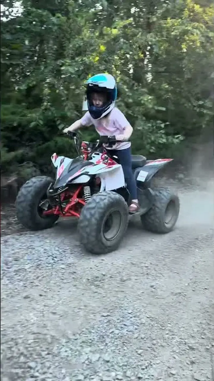 A child in a helmet riding a small quad along a dirt track.