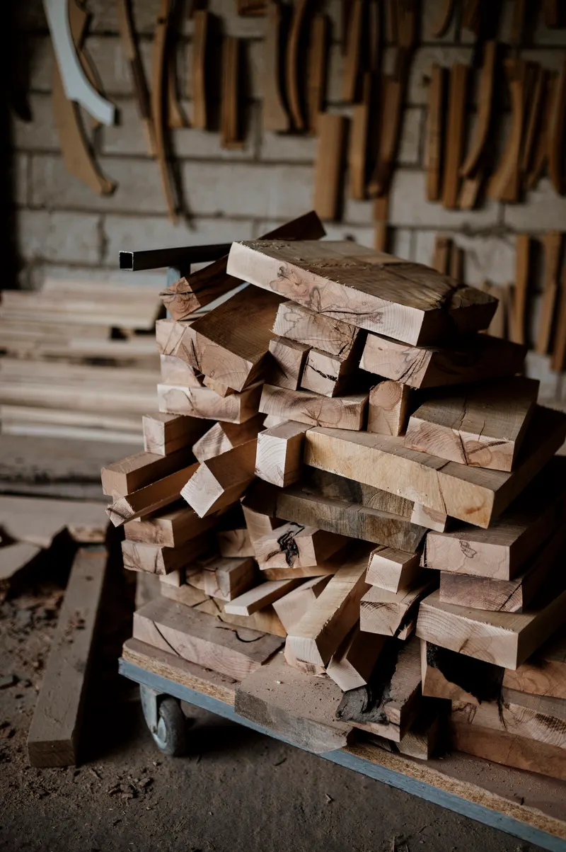A cart stacked with rough-sawn hardwood blanks in a workshop, hand-tool patterns hanging on the block wall behind it